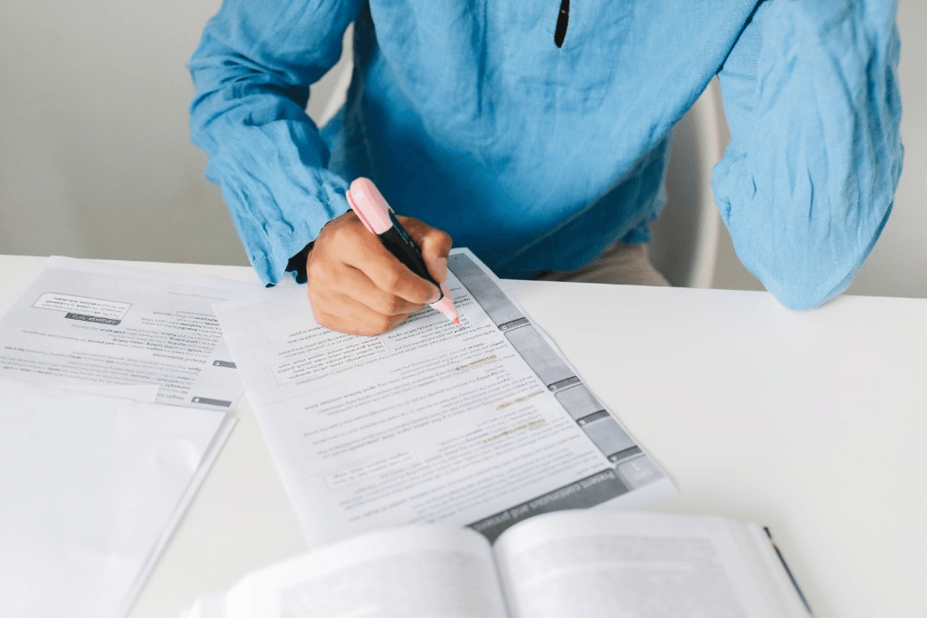 Person highlighting notes on a printed worksheet beside an open book on a desk